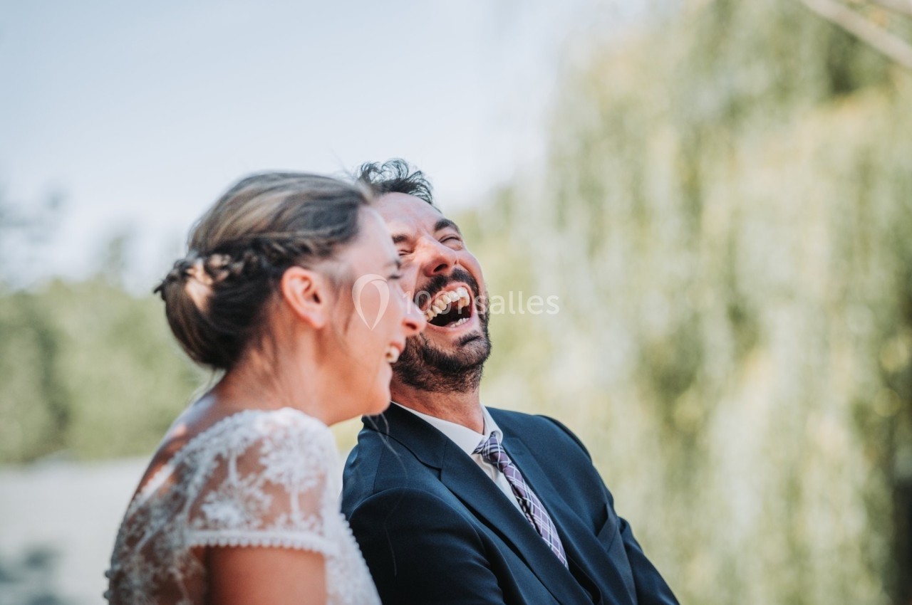 Un couple souriant et riant en extérieur, avec un arrière-plan flou de verdure.