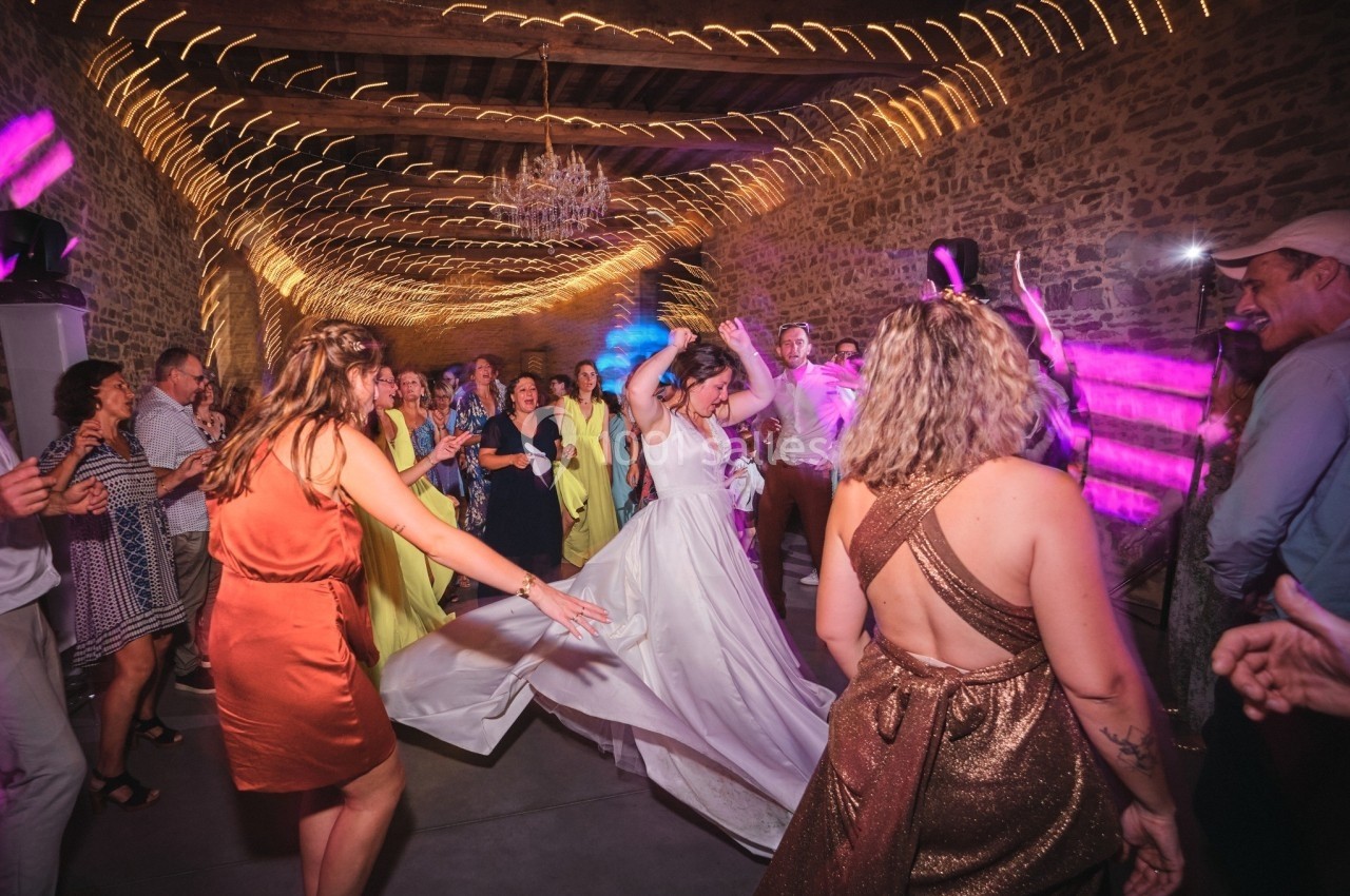 Des invités dansent lors d'une fête dans une salle en pierre illuminée de guirlandes et de lumières colorées.