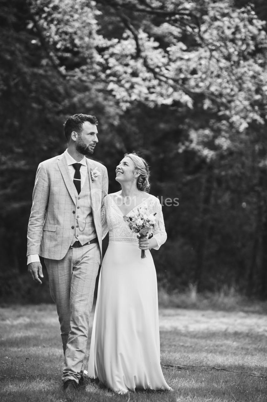 Un couple de mariés marche dans un parc, souriant et échangeant un regard complice.