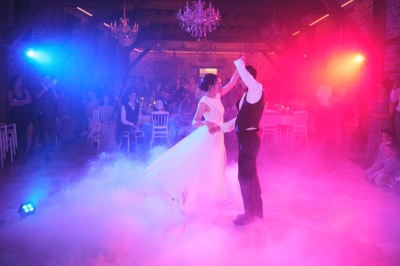 Un couple danse sous des lumières colorées et une ambiance de fumée lors d'une réception festive.