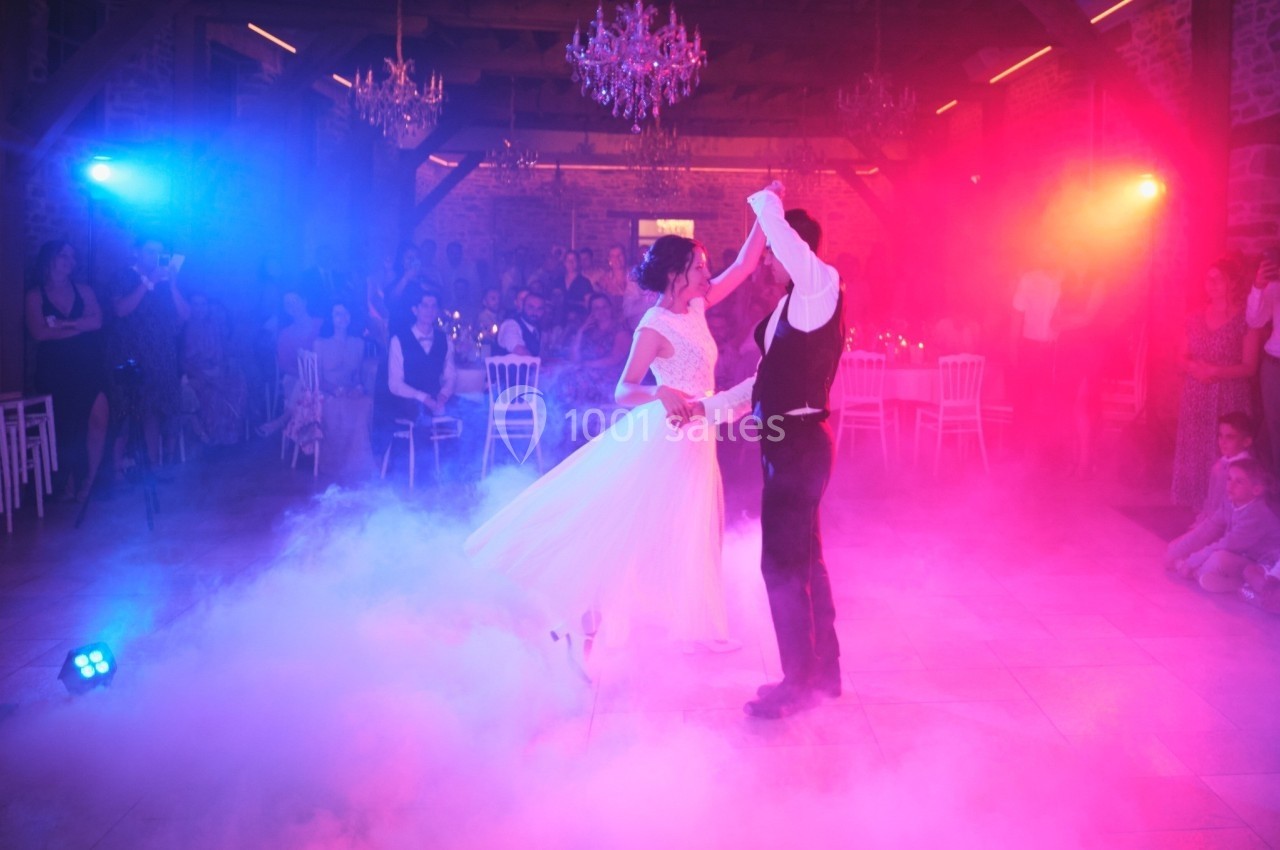 Un couple danse sous des lumières colorées et une ambiance de fumée lors d'une réception festive.