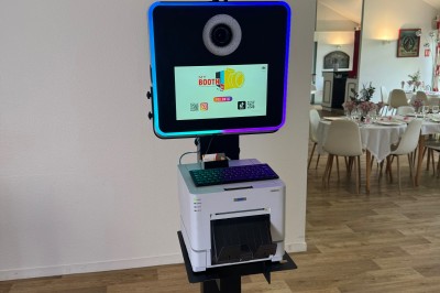 Borne photo interactive avec écran, éclairage circulaire et imprimante intégrée, installée dans une salle lumineuse.