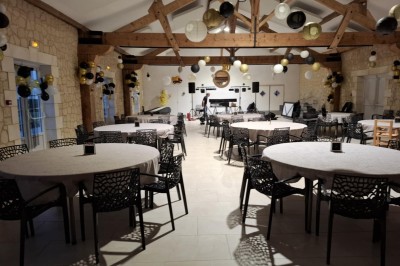 Salle de réception décorée pour un anniversaire, avec tables alignées, guirlandes et lanternes suspendues au plafond en bois.