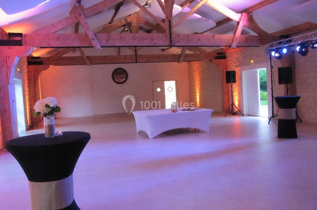 Salle de réception lumineuse avec poutres apparentes, tables hautes noires et éclairage d'ambiance chaleureux.