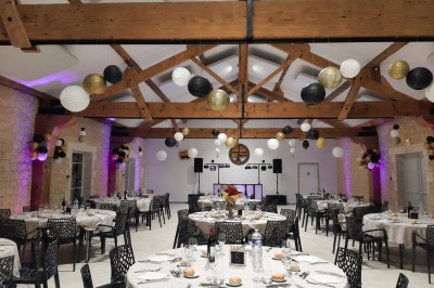 Salle de réception décorée pour un anniversaire, avec tables alignées, guirlandes et lanternes suspendues au plafond en bois.