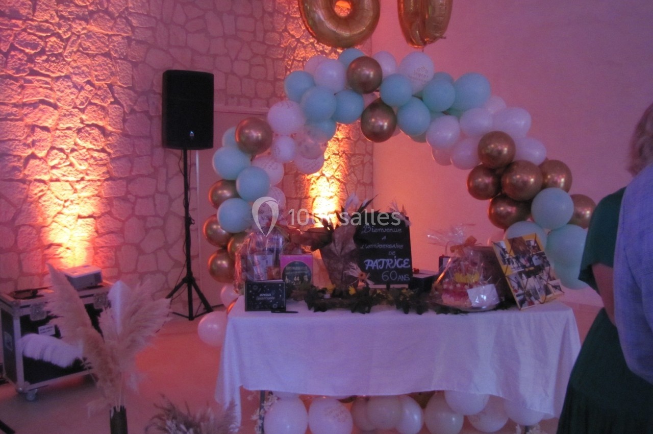 Décoration de fête avec arche de ballons blancs, dorés et bleus, table ornée de cadeaux et panneau indiquant 60 ans.