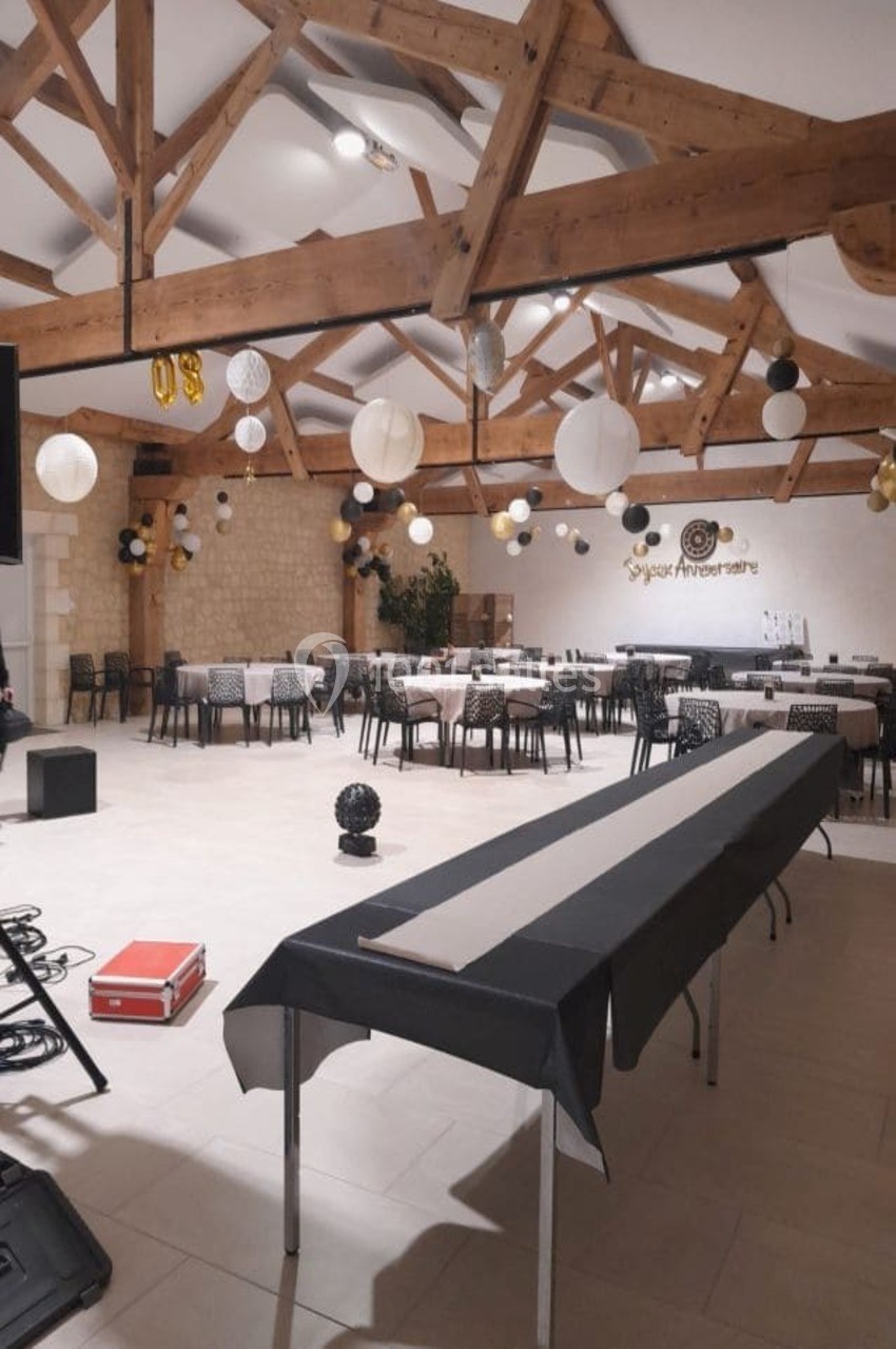 Salle décorée pour un anniversaire avec tables alignées, nappes noires et blanches, et lanternes suspendues au plafond en…