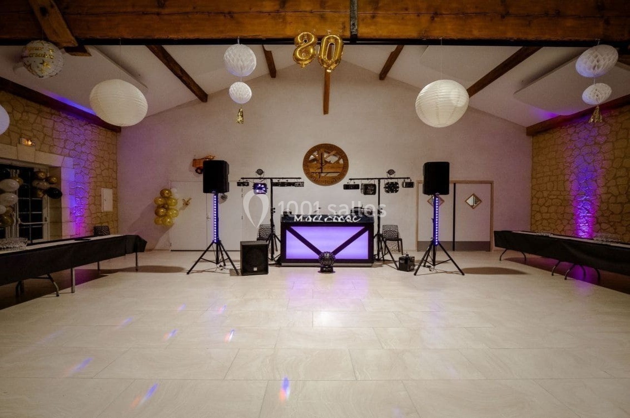 Salle de réception décorée avec des guirlandes lumineuses, des ballons dorés et une table de DJ au centre.