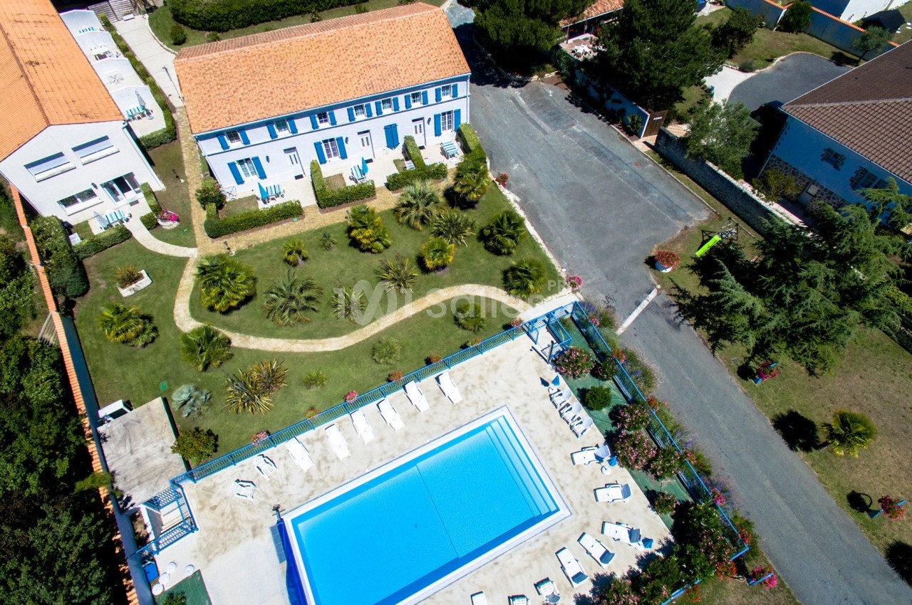 Vue aérienne d'une résidence avec jardin paysager, piscine extérieure et chaises longues disposées autour.