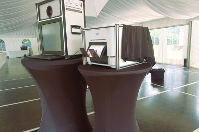 Borne photo avec éclairage, clavier et imprimante posée sur des tables noires dans un espace intérieur.