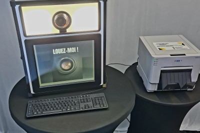 Borne photo avec éclairage, clavier et imprimante posée sur des tables noires dans un espace intérieur.