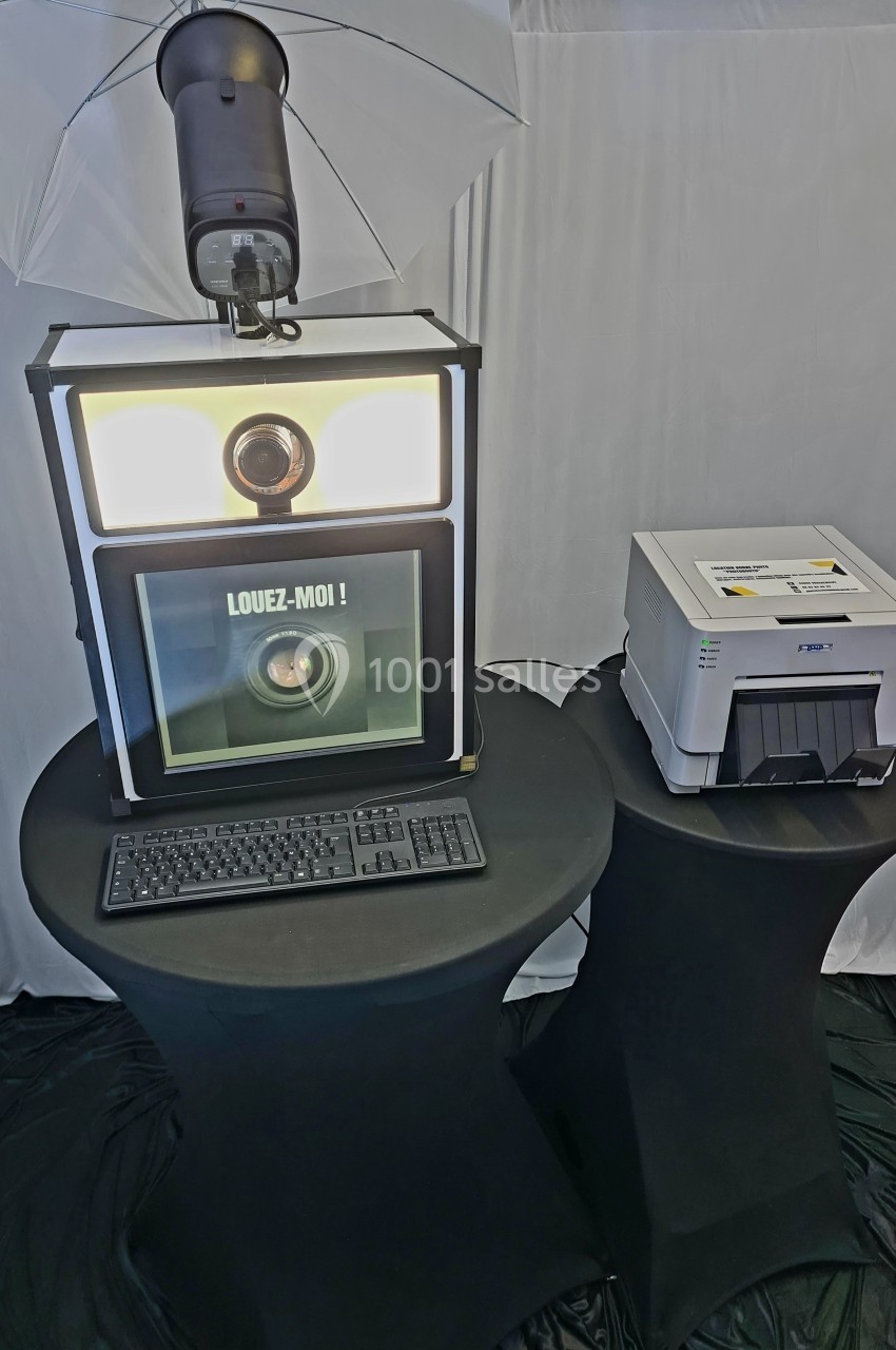 Borne photo avec éclairage, clavier et imprimante posée sur des tables noires dans un espace intérieur.