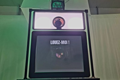 Borne photo avec éclairage, clavier et imprimante posée sur des tables noires dans un espace intérieur.