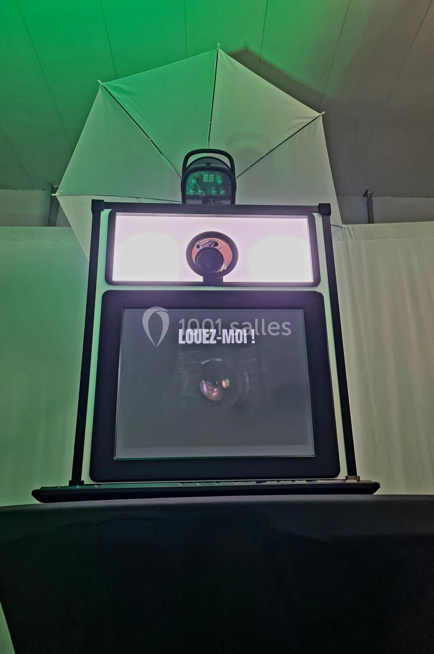 Borne photo avec écran affichant ’Louez-moi !’ et éclairage LED, posée devant un fond blanc avec un parapluie lumineux.