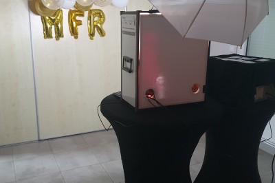 Borne photo rétro-éclairée dans une salle décorée avec des ballons ’25’ et un éclairage violet.