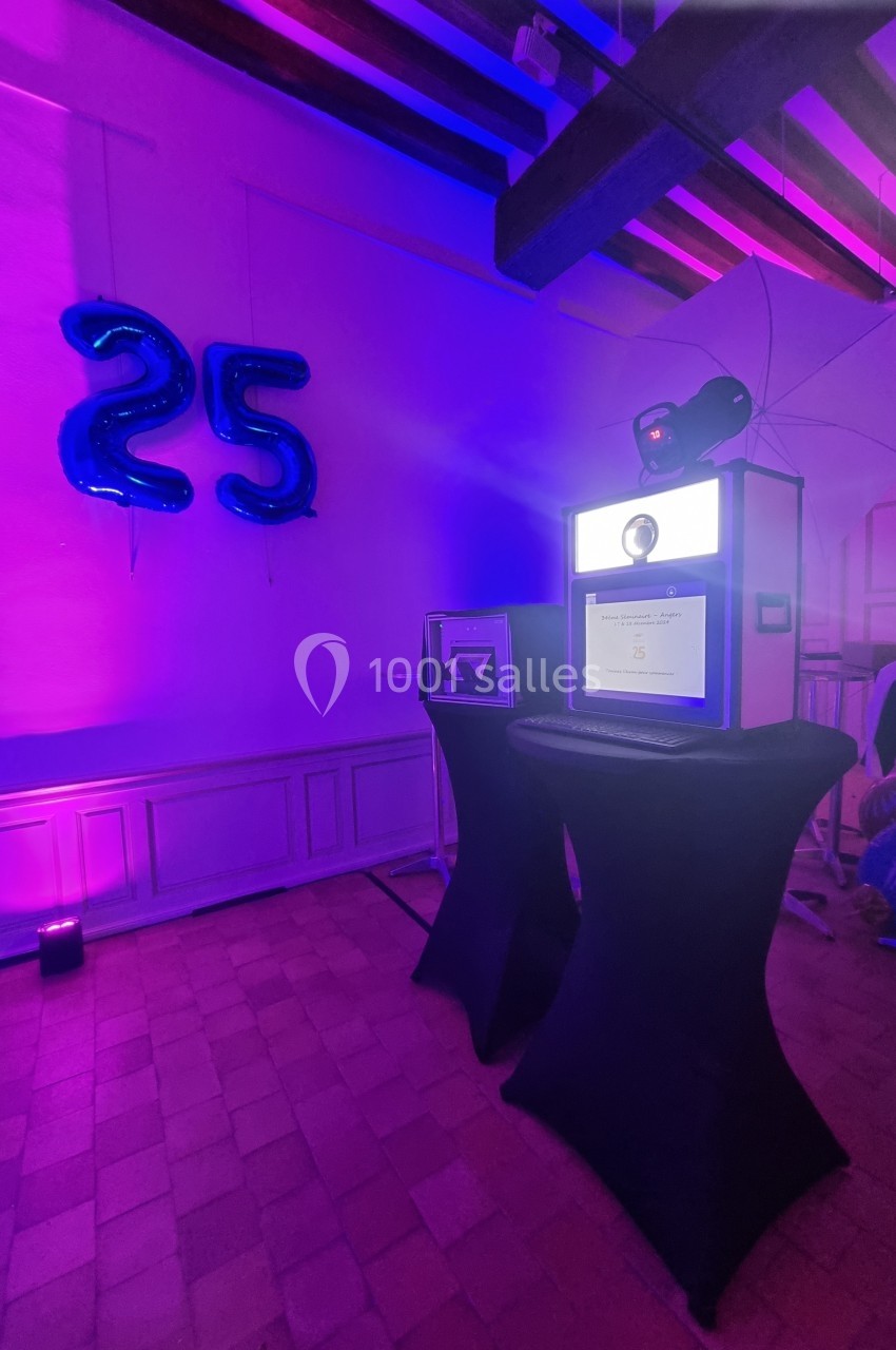 Borne photo rétro-éclairée dans une salle décorée avec des ballons ’25’ et un éclairage violet.