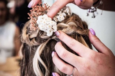 Coiffure de cheveux blonds bouclés ornée de fleurs, ajustée par une personne avec des ongles vernis violets.