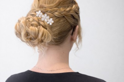 Coiffure de cheveux blonds bouclés ornée de fleurs, ajustée par une personne avec des ongles vernis violets.