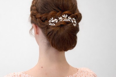Coiffure de cheveux blonds bouclés ornée de fleurs, ajustée par une personne avec des ongles vernis violets.