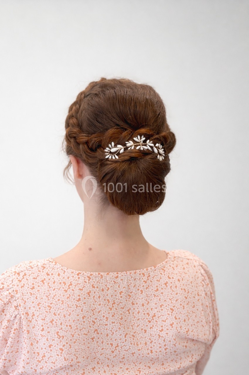 Femme de dos avec un chignon tressé orné de petites fleurs blanches, portant une robe à motifs discrets.