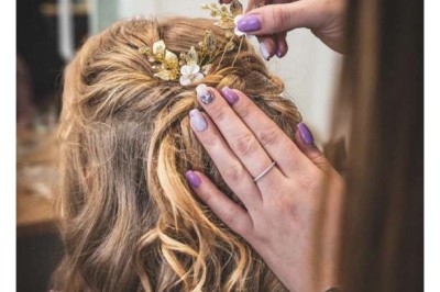 Coiffure de cheveux blonds bouclés ornée de fleurs, ajustée par une personne avec des ongles vernis violets.
