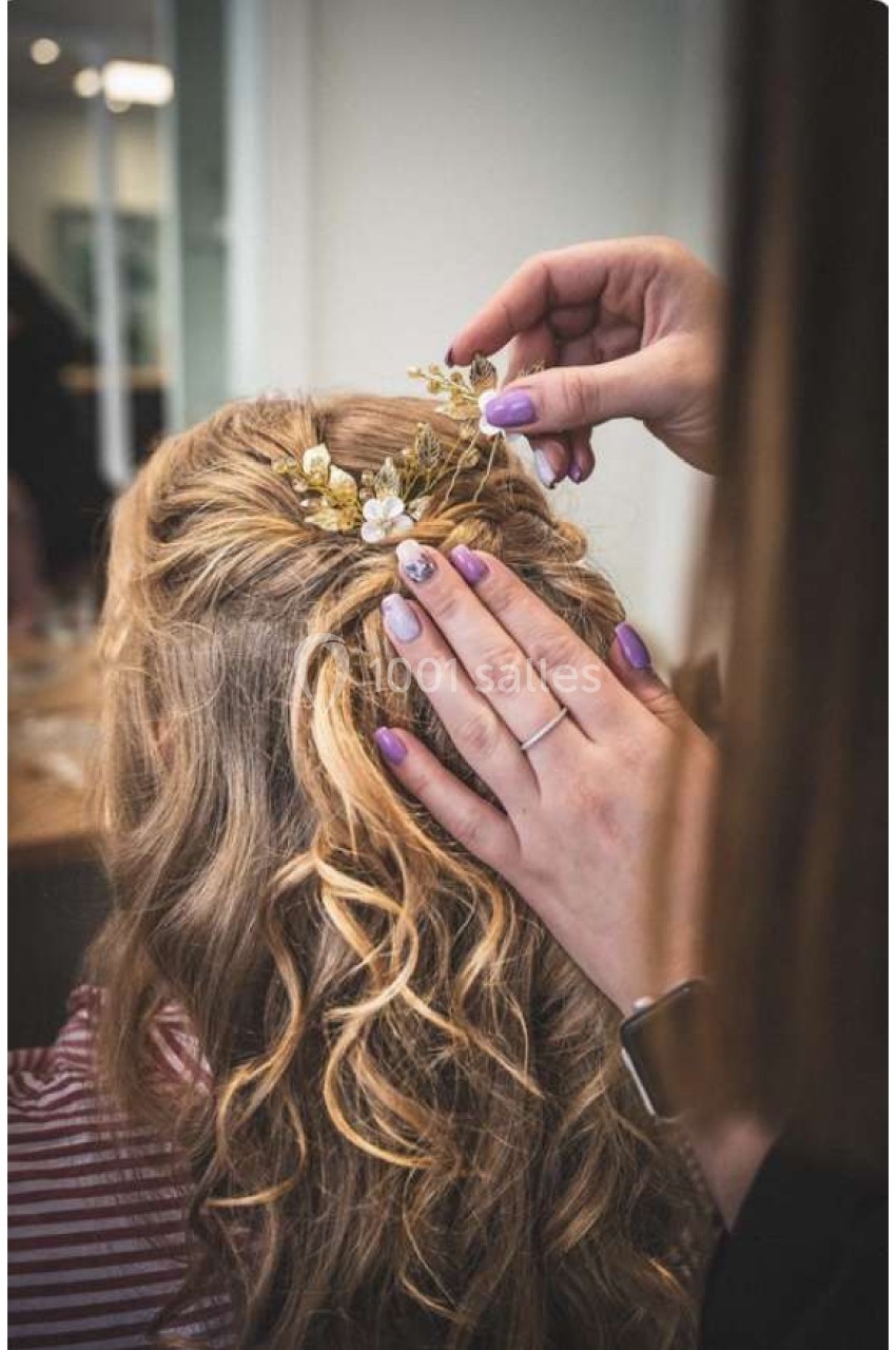 Coiffure de cheveux blonds bouclés ornée de fleurs, ajustée par une personne avec des ongles vernis violets.