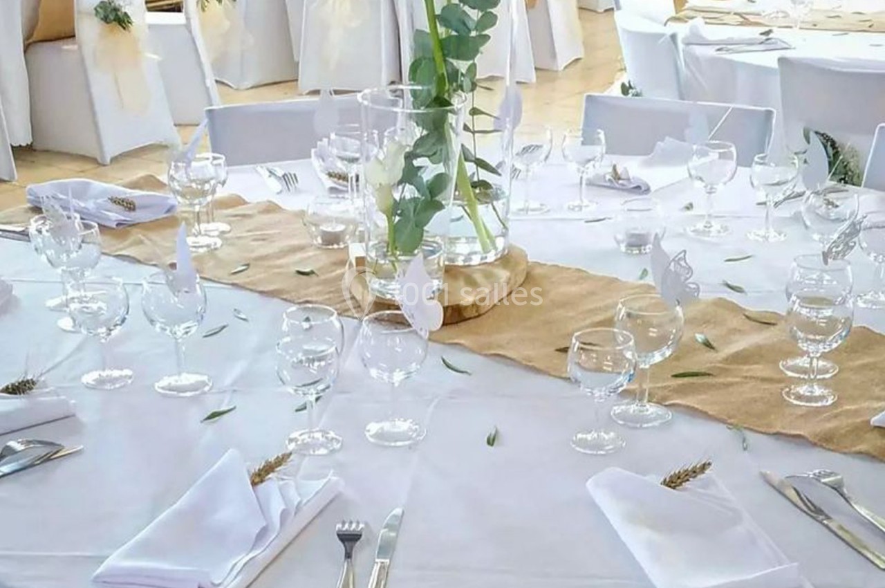 Table décorée pour un événement avec nappes blanches, chemins de table en jute, verres, couverts et centre de table floral.