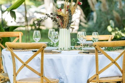 Miniature Mas Adamon Location #18 Table dressée en extérieur avec nappes blanches, verres et décorations florales, entourée de chaises en bois.