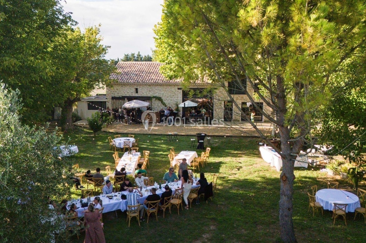 Vue d'un jardin avec des tables dressées et des invités lors d'un événement en plein air devant un bâtiment en pierre.