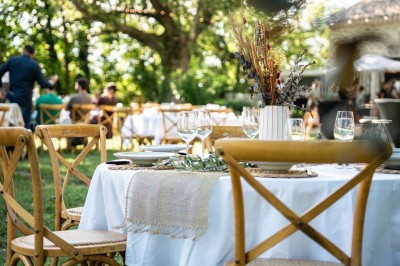 Miniature Mas Adamon Location #36 Table dressée en extérieur avec nappes blanches, verres et décorations florales, entourée de chaises en bois.
