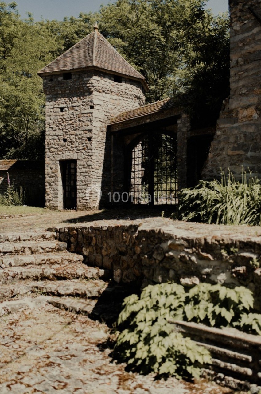 Vieille tour en pierre avec un toit en pente, entourée de verdure et d'un escalier en pierre au premier plan.