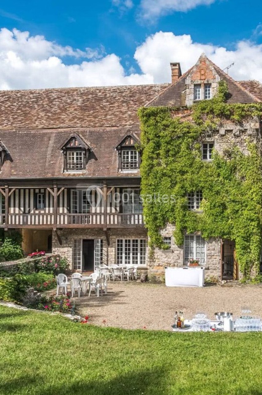 Façade d'une grande maison en pierre avec toit en tuiles, lierre grimpant et jardin aménagé devant.