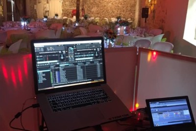 Salle de réception décorée avec des guirlandes lumineuses, tables rondes dressées et chaises blanches.