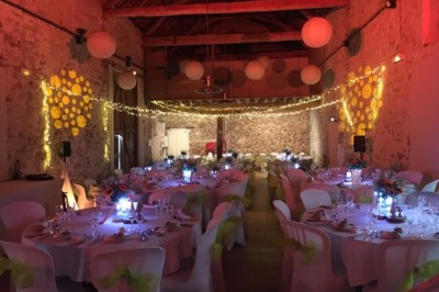 Salle de réception décorée avec des guirlandes lumineuses, tables rondes dressées et chaises blanches.