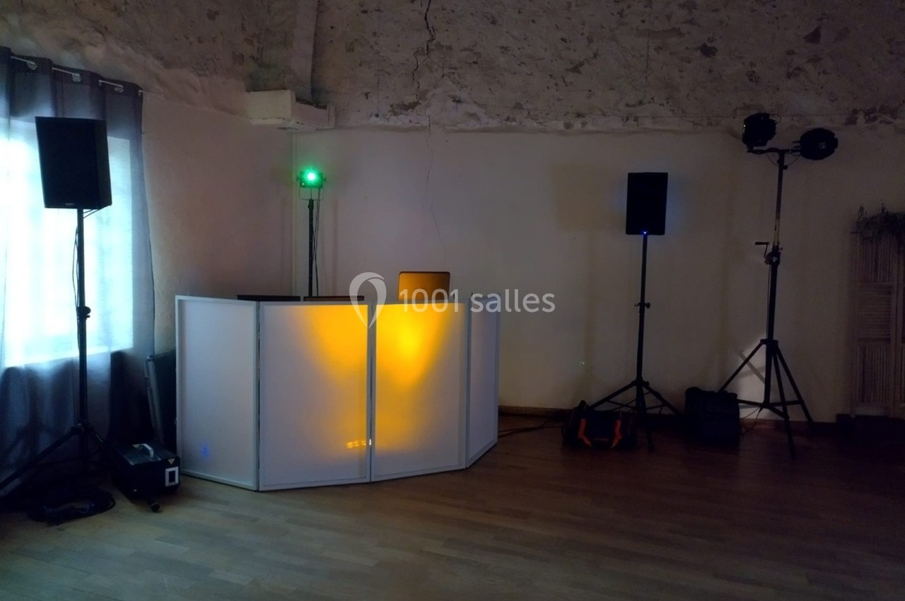 Console de DJ éclairée en orange dans une salle avec murs en pierre, haut-parleurs et projecteurs installés.