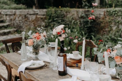 Salle de réception décorée avec des guirlandes lumineuses, tables rondes dressées et chaises blanches.