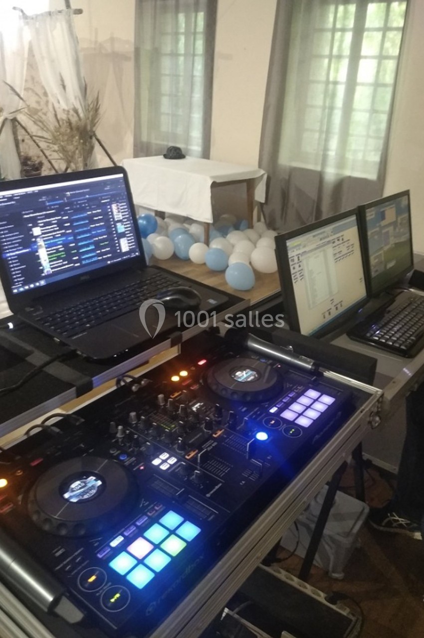 Deux ordinateurs portables et une table de mixage DJ installés sur une table, entourés de ballons et d'équipements.