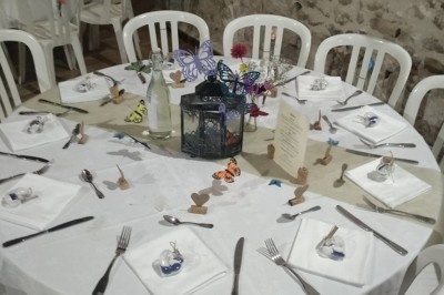 Salle de réception décorée avec des guirlandes lumineuses, tables rondes dressées et chaises blanches.