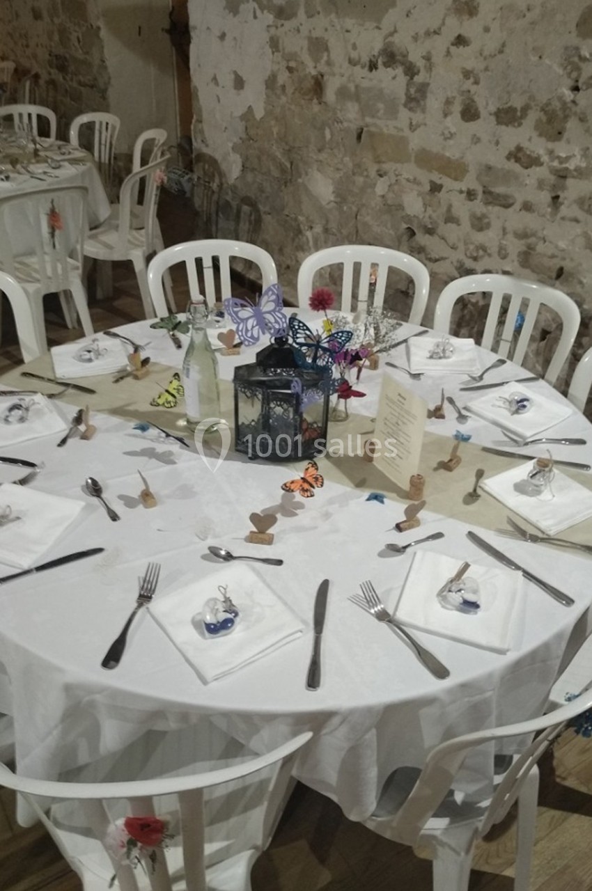 Table ronde décorée pour un événement, avec nappes blanches, couverts disposés, lanternes et papillons colorés.