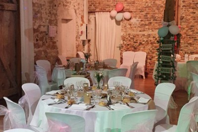 Salle de réception décorée avec des guirlandes lumineuses, tables rondes dressées et chaises blanches.