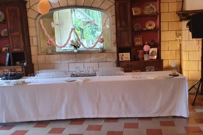 Salle de réception décorée avec des guirlandes lumineuses, tables rondes dressées et chaises blanches.
