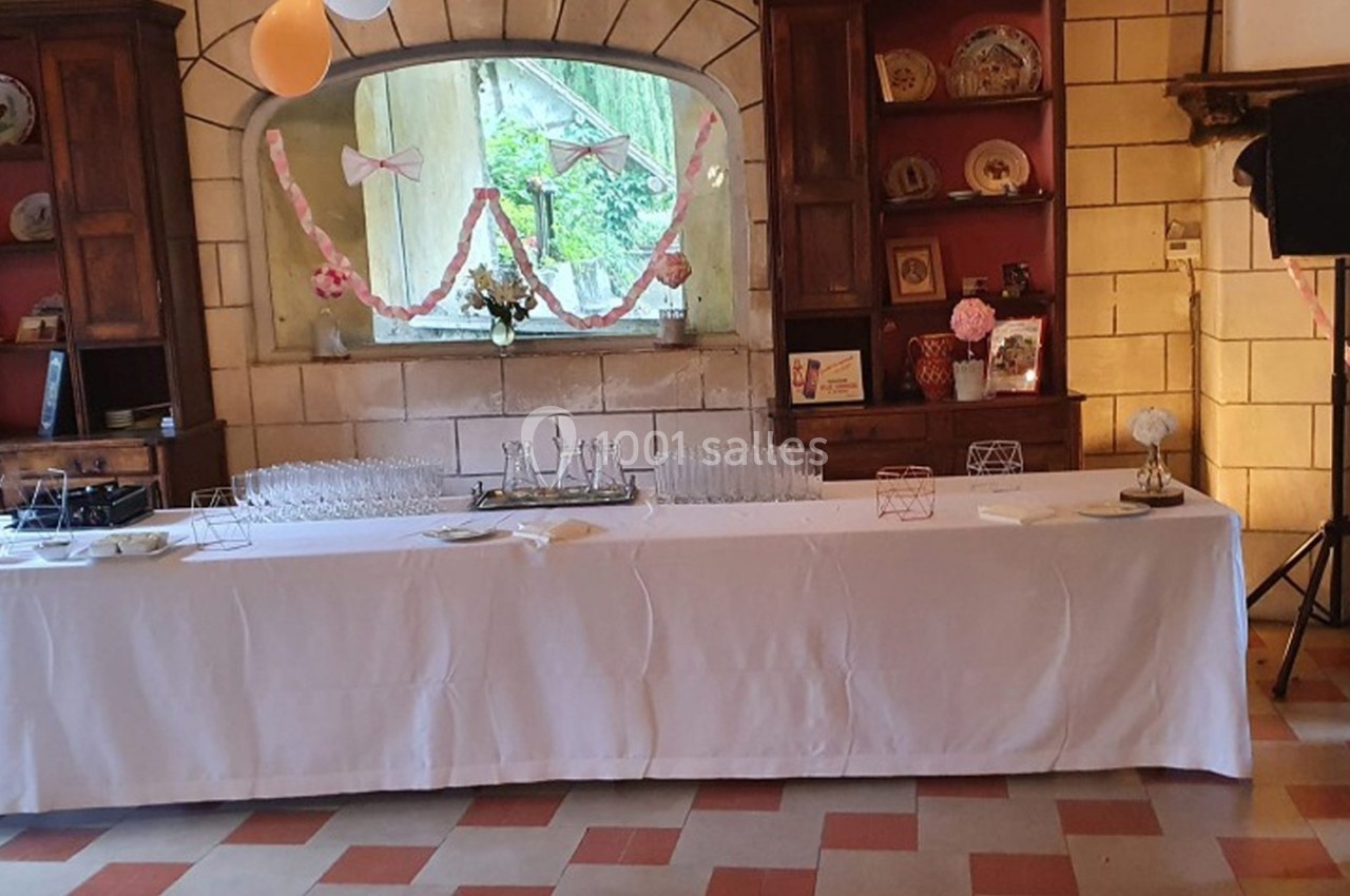 Table dressée avec une nappe blanche, verres et décorations roses dans une salle au style rustique avec des étagères en bois.