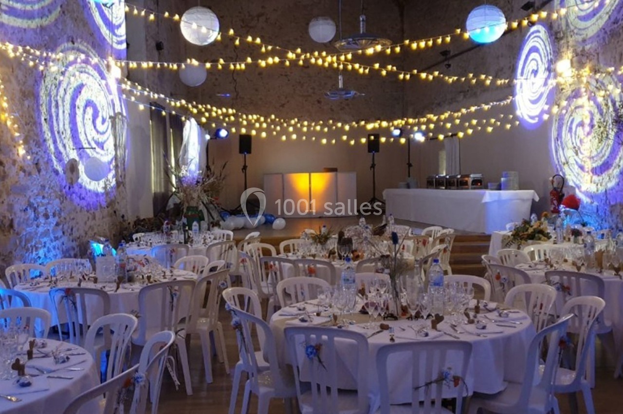 Salle de réception décorée avec des guirlandes lumineuses, des tables dressées et des projections colorées sur les murs.