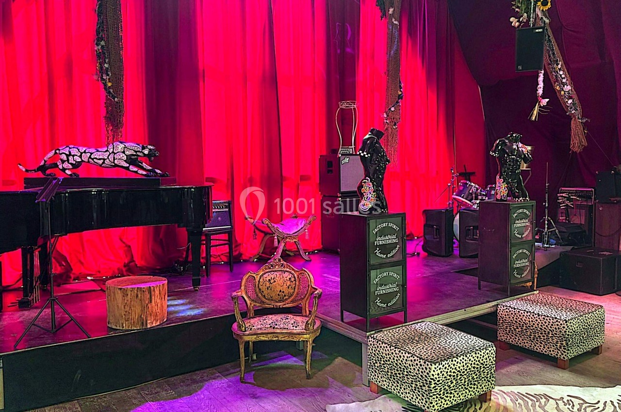 Scène décorée avec rideaux rouges, piano à queue, fauteuils et éléments à motifs animaliers.