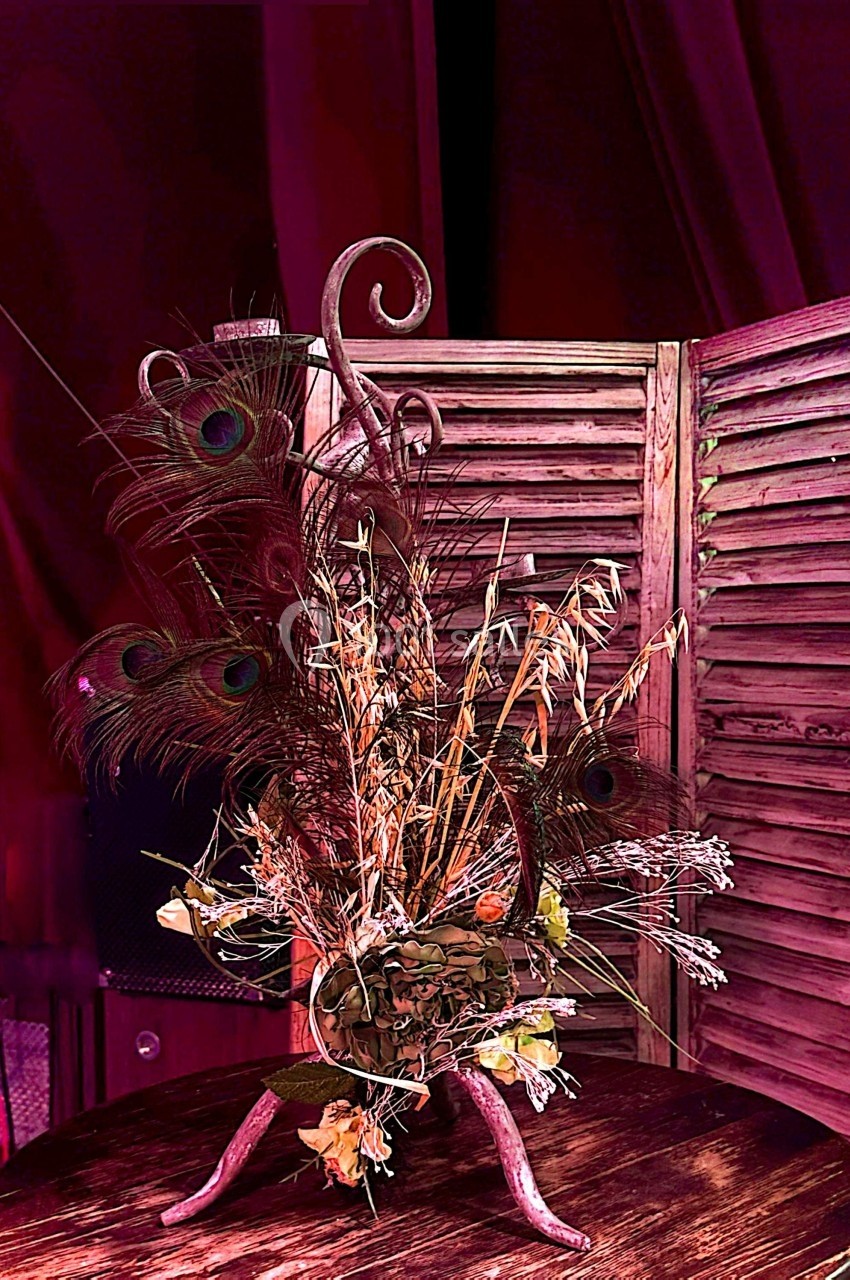Arrangement floral avec plumes de paon et branches séchées dans un vase décoratif, posé sur une table en bois devant un…