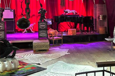 Buste masculin noir sans tête, orné de motifs colorés, exposé devant un rideau rouge et un piano en arrière-plan.