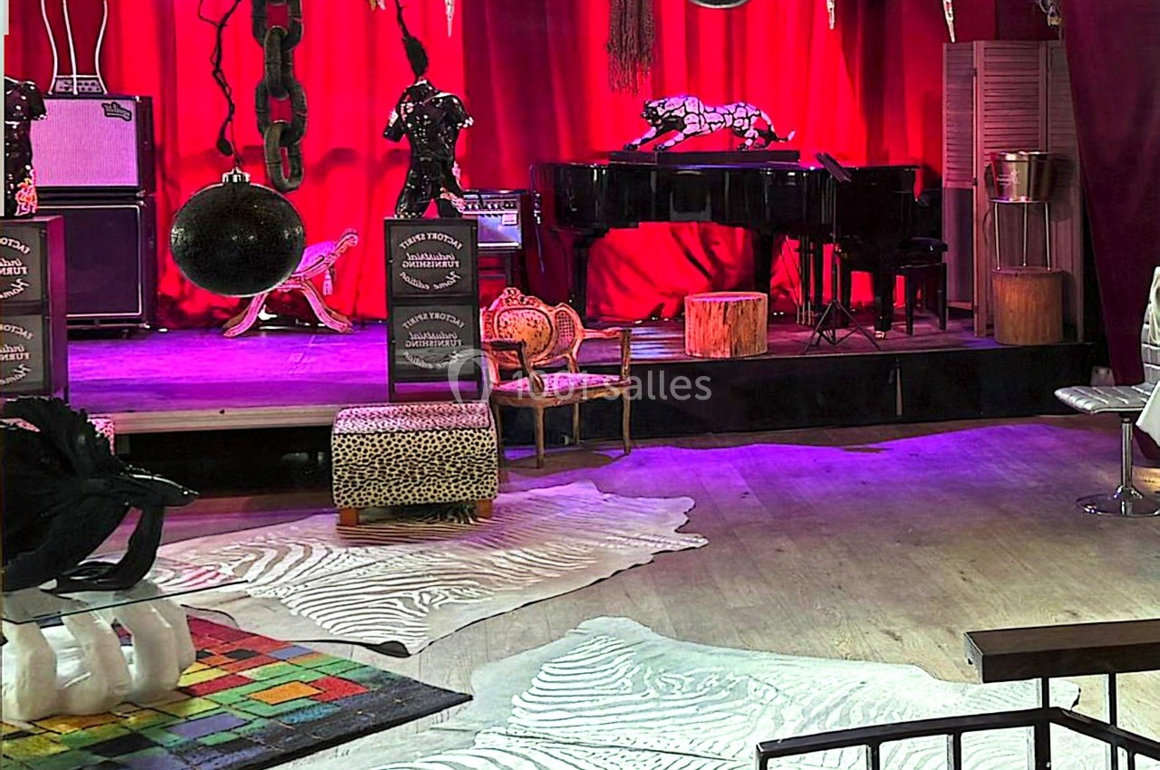 Scène avec rideaux rouges, piano noir, fauteuils éclectiques et décorations variées dans une ambiance artistique.