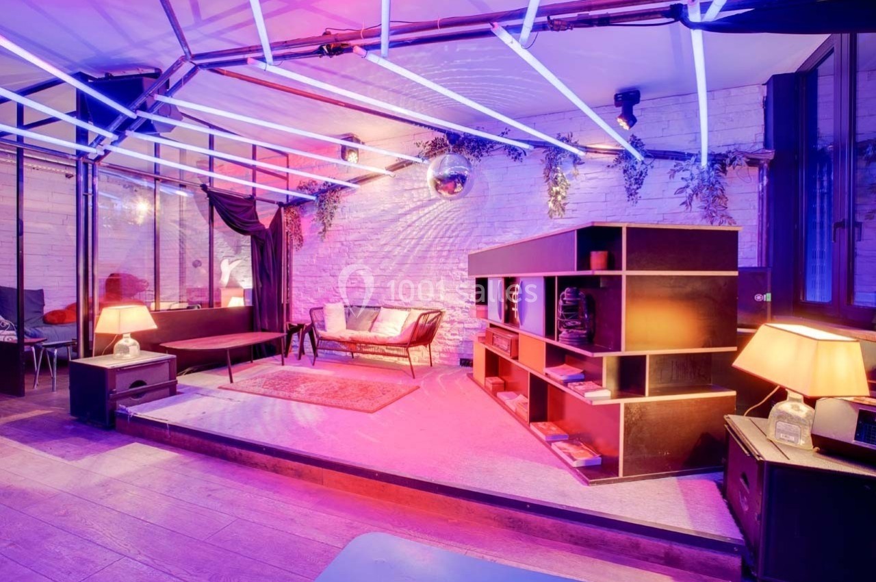 Salle moderne avec éclairage néon violet, canapé en cuir, étagères en bois et décorations murales.