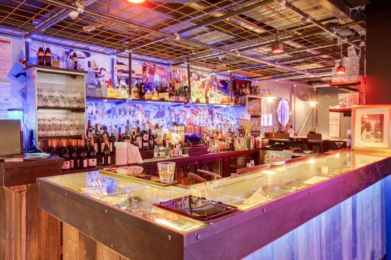 Bar avec comptoir éclairé, étagères remplies de bouteilles et ambiance lumineuse colorée.