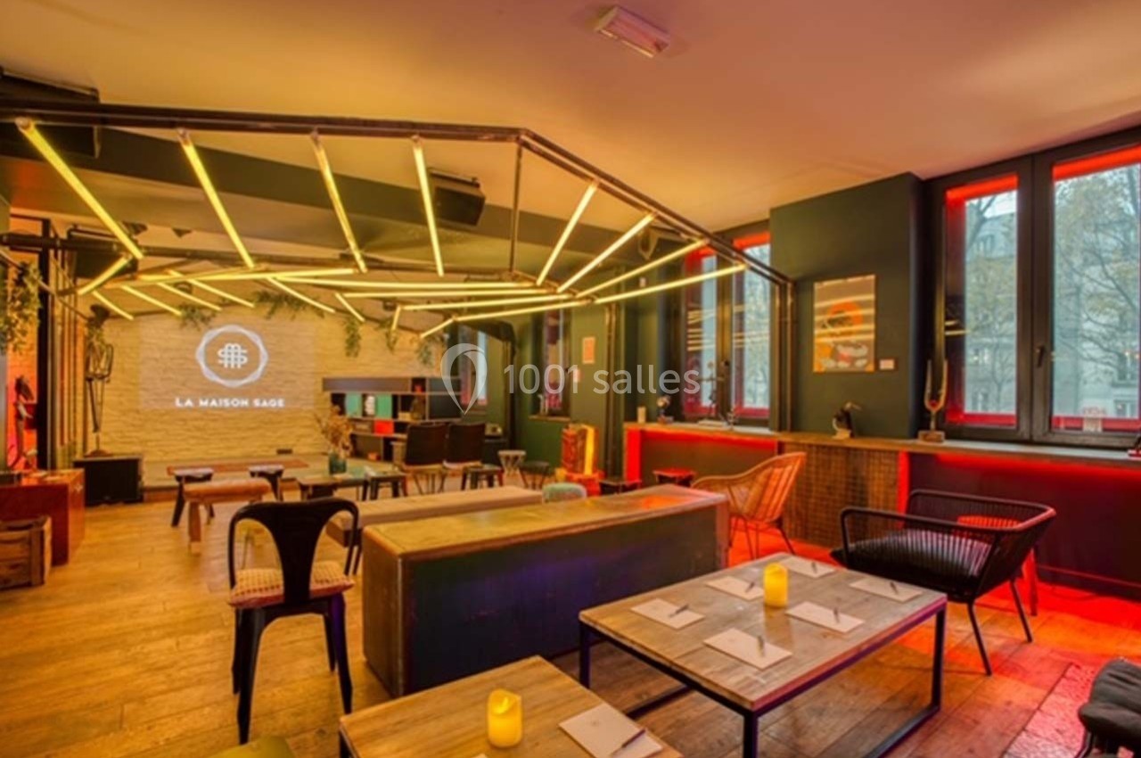 Salle moderne avec tables dressées, éclairage chaleureux, murs en briques et grandes fenêtres donnant sur l'extérieur.